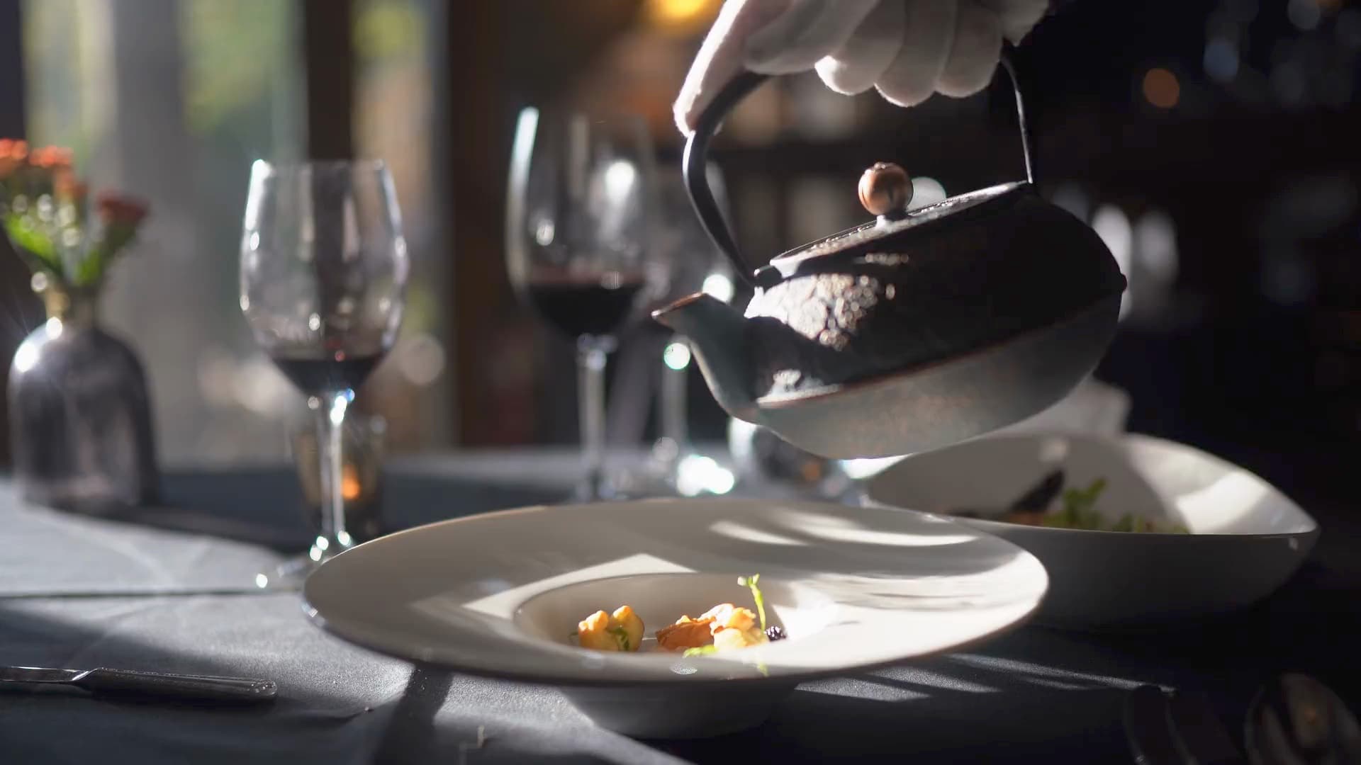 A chef finishes a fine-dining dish beside a glass of red wine